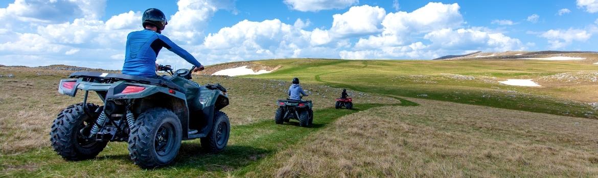 three people ride their own ATV on a grass trail on rolling hills