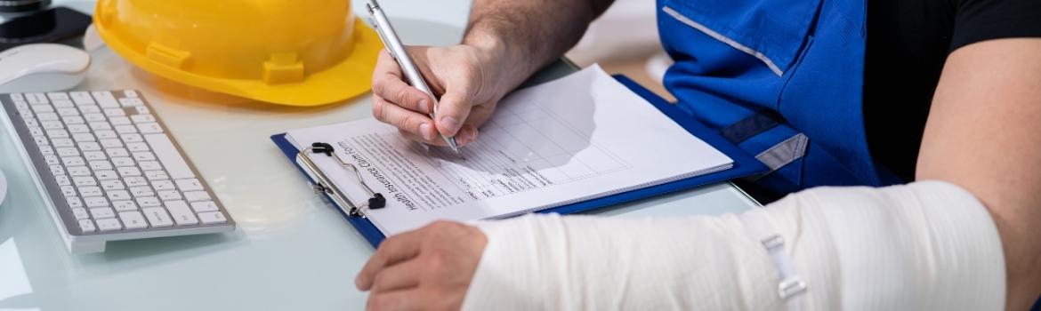 a man wearing a white nylon wrap on his left arm signs a paper in a blue clipboard for a health insurance claim